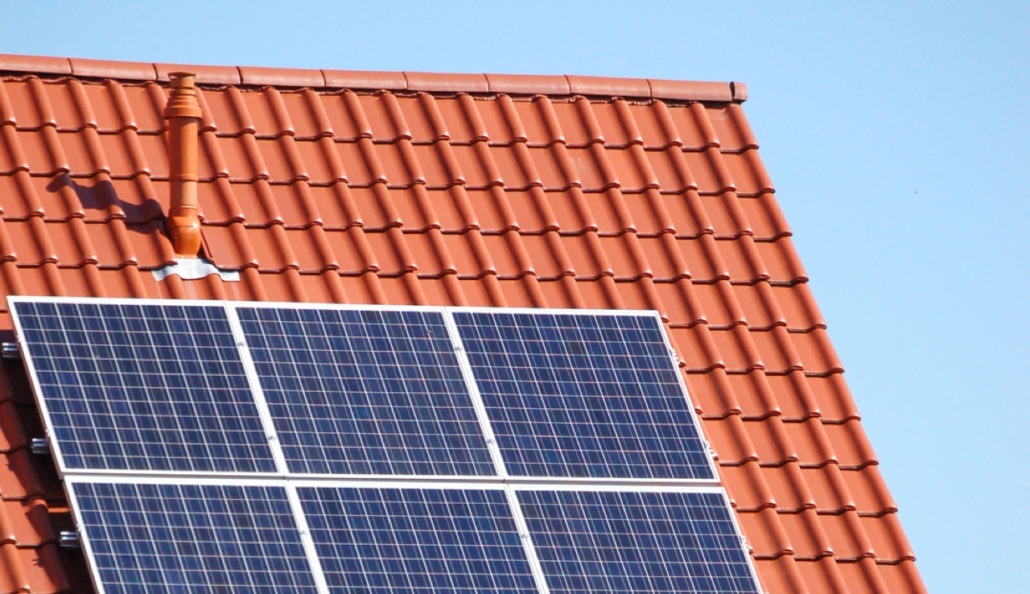 640x369-oekostrom-solarenergie Vor einem strahlend blauen Himmel glänzen Solarpanele der oekostrom AG auf einem roten Ziegeldach.