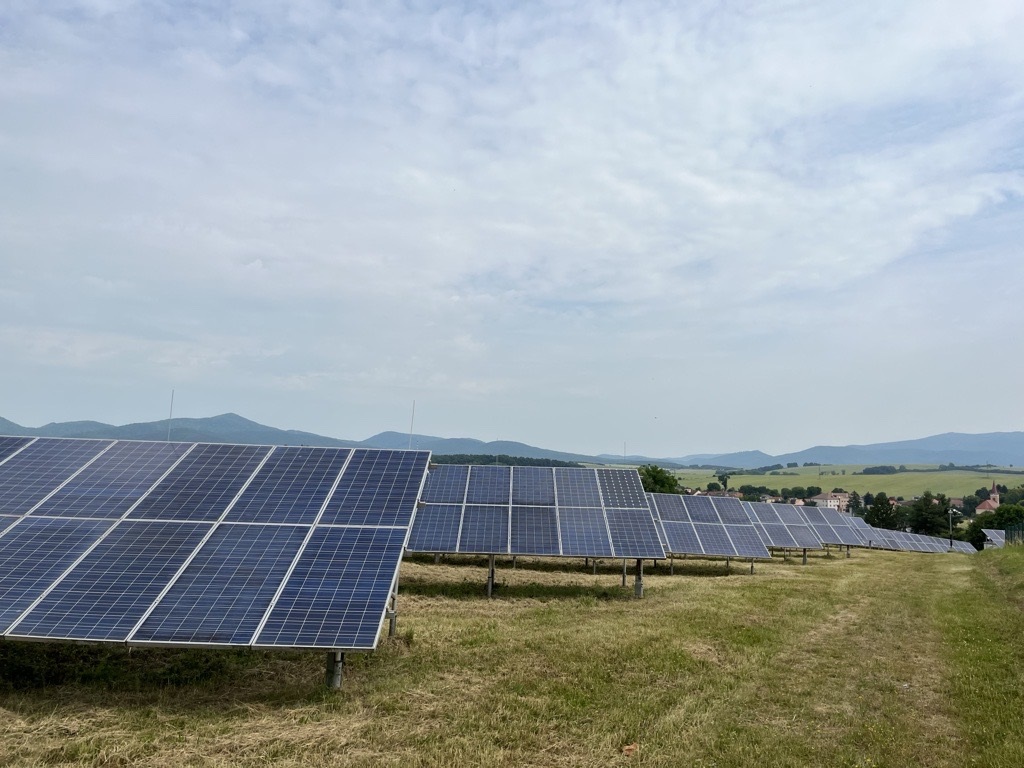 oekostrom AG: Vor dem Hintergrund entfernter Hügel und eines bewölkten Himmels ist ein Feld aus Solarmodulen in Reihen aufgestellt.