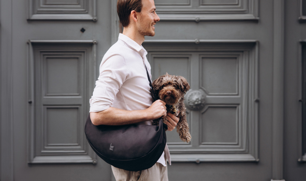Mann mit GOT BAG Tasche und Hund auf dem Arm vor einer Haustüre