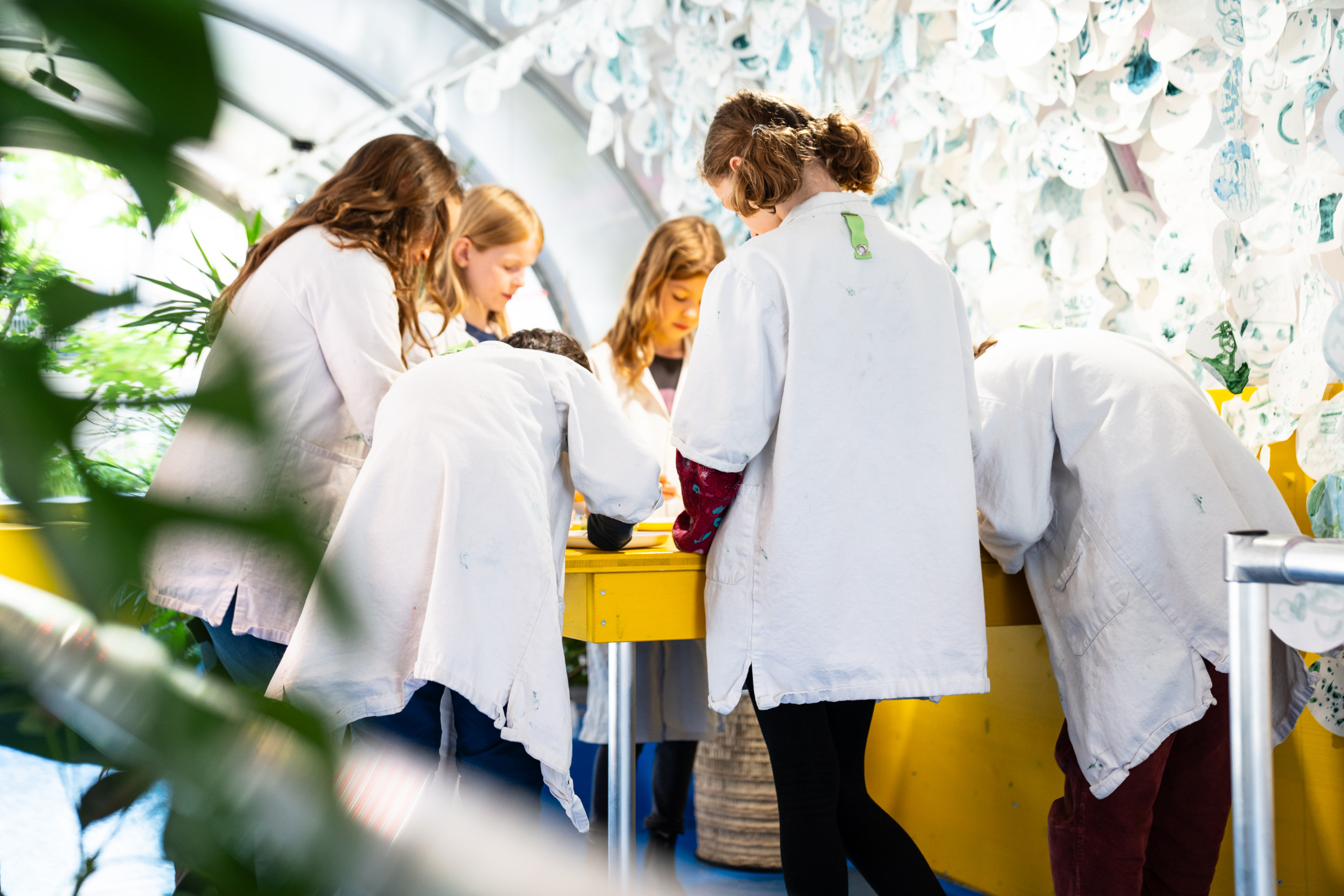 Kinder tragen einen weißen Forscherkittel und sehen durch ein Mikroskop im ZOOM Kindermuseum