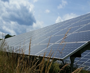 oekostrom AG: Eine Solarzellenanlage auf einer Wiese unter einem teilweise bewölkten Himmel.