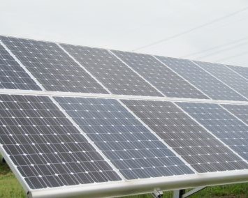 oekostrom AG: Eine Nahaufnahme einer Solarzellenanordnung, die mehrere in einem Gittermuster angeordnete Photovoltaikzellen vor einem bewölkten Himmel zeigt.