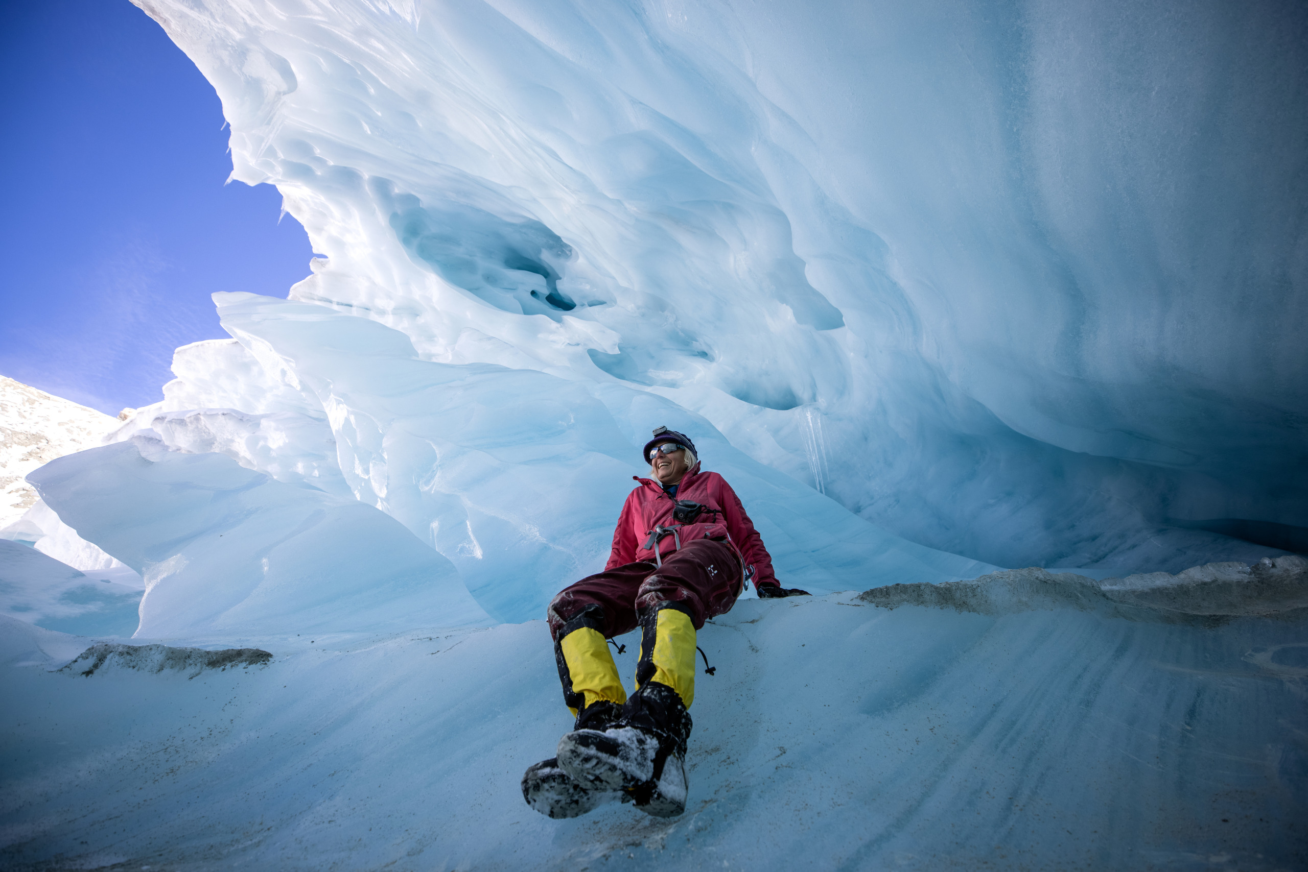 Eingehüllt in Winterkleidung sitzt eine Person neben einer Eishöhle mit blauen und weißen Eisformationen über dem Kopf und ist sich der Prinzipien der Kreislaufwirtschaft bewusst. Umgeben von den Wundern der Natur denkt sie darüber nach, wie Recycling und Klimaschutzmaßnahmen diese unberührte Schönheit für zukünftige Generationen bewahren können.