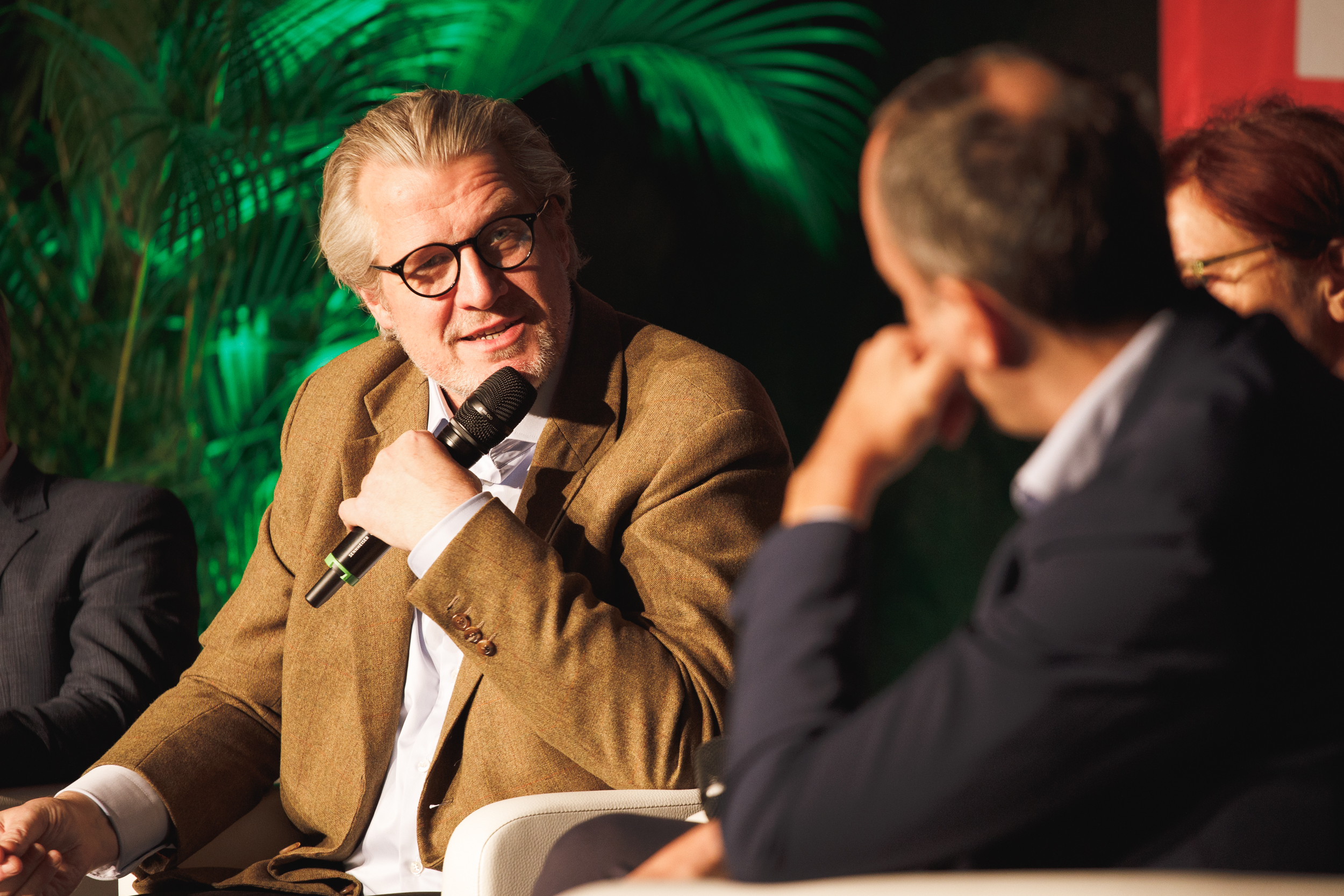 Ein Mann mit Brille und grauem Haar spricht in ein Mikrofon, während er in einer schwach beleuchteten Campus-Umgebung an einer Podiumsdiskussion über grüne Innovationen teilnimmt, darunter auch die Rolle der Ökostrom AG.