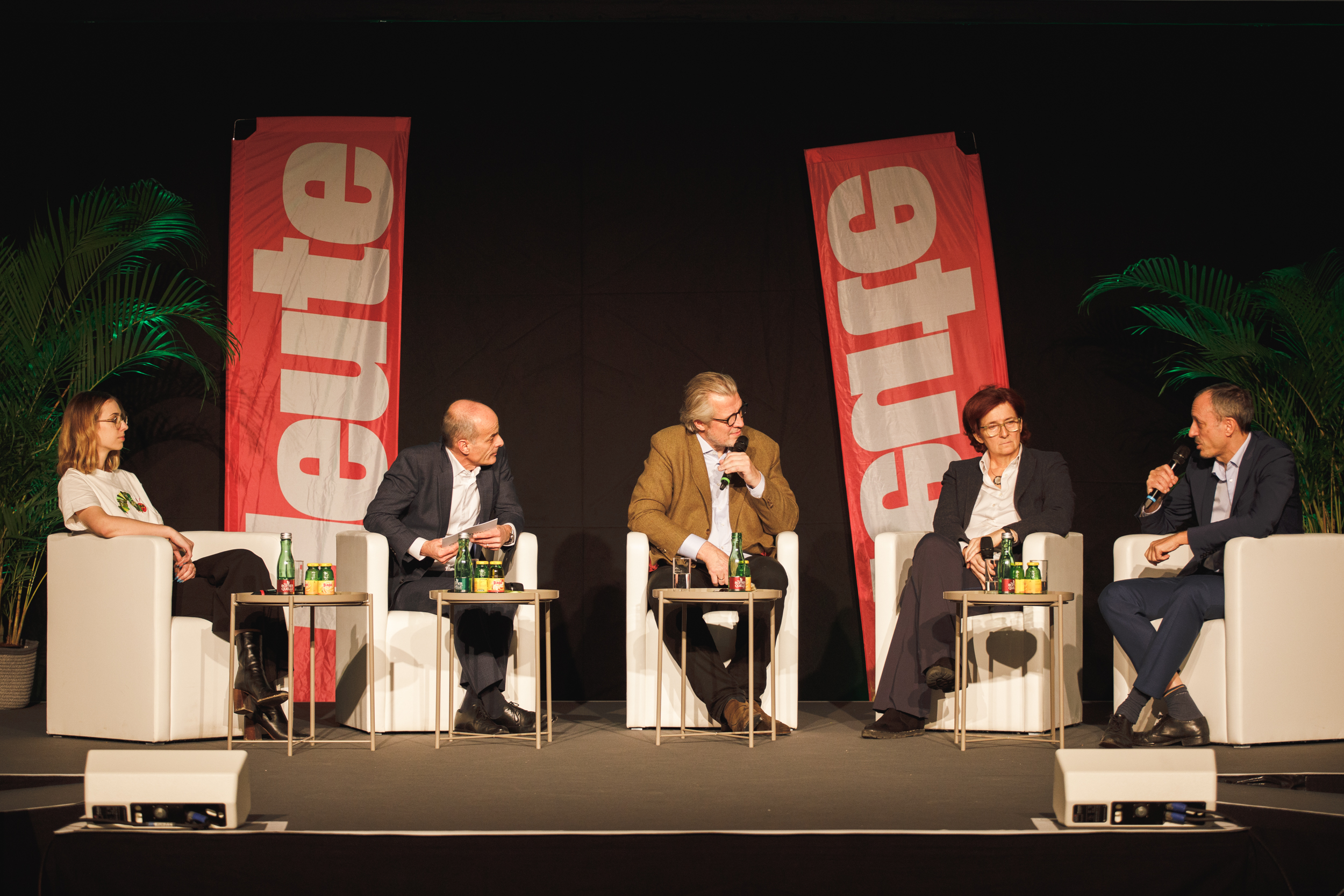 Fünf Personen sitzen auf einer Bühne und diskutieren über Nachhaltigkeit. Im Hintergrund sind zwei Banner mit der Aufschrift „teute“ in roter Schrift und „oekostrom AG am Campus“ prominent platziert, die den Fokus auf umweltfreundliche Energielösungen betonen.