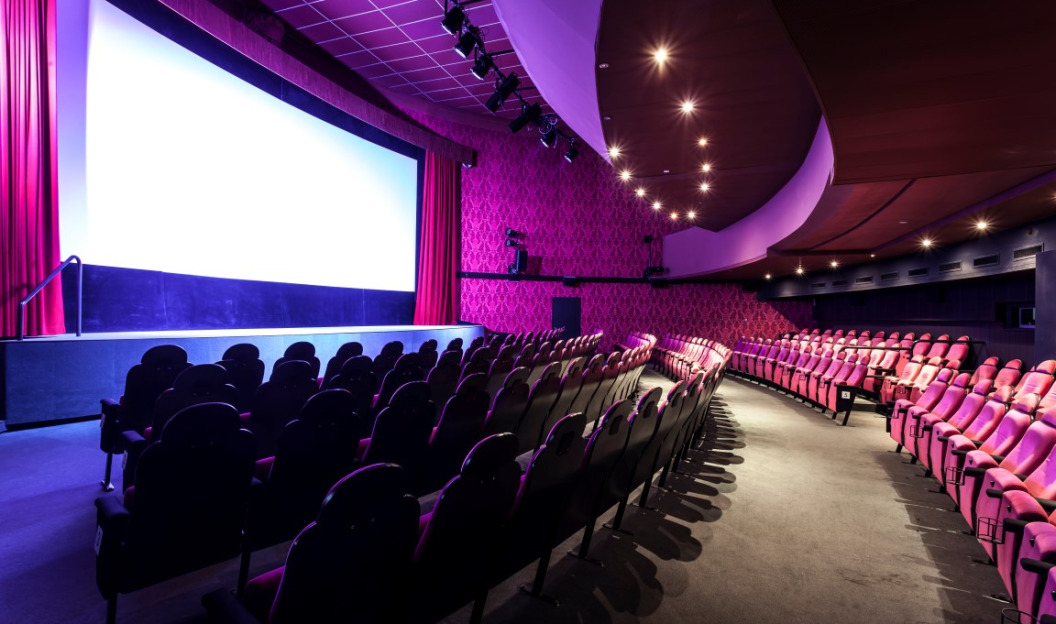 Das Kino erinnert an das Cinema Paradiso und bietet Reihen roter Sitze vor einer großen Leinwand. Die roten Stoffwände sorgen für Wärme, während die Deckenbeleuchtung eine gemütliche Atmosphäre schafft. Dieses Kino setzt auf Nachhaltigkeit und verwendet Ökostrom, um ein umweltfreundliches Kinoerlebnis zu gewährleisten.