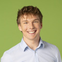 Junger Mann mit hellbraunem Haar, der ein hellblaues Button-up-Hemd trägt und vor einem schlichten grünen Hintergrund lächelt.