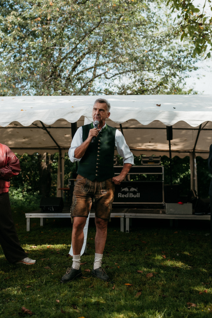 Ein Mann in bayerischer Tracht spricht auf dem Eröffnungsfest St. Veit in ein Mikrofon. Er steht vor einem weißen Zelt, hinter dem eine Tonanlage zu sehen ist.