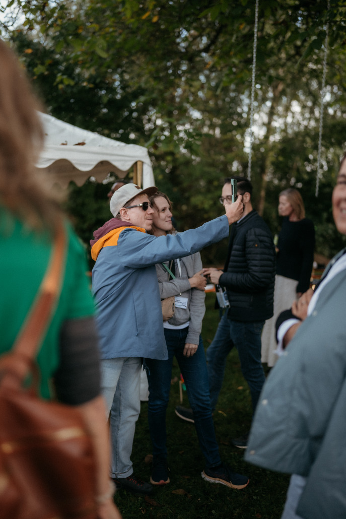 Eine Gruppe von Menschen steht draußen in der Nähe eines Zeltes auf dem Eröffnungsfest St. Veit; eine Person mit Sonnenbrille und Kappe hält ein Handy hoch und scheint ein Selfie zu machen.
