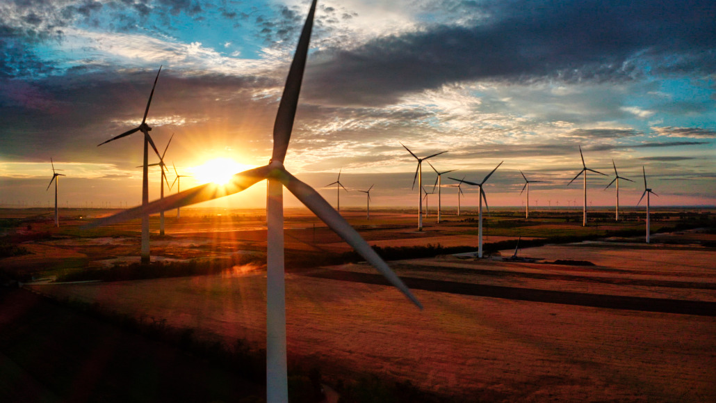 Screenshot Windturbinen in einer ländlichen Landschaft, wenn die Sonne hinter den Wolken untergeht, Licht auf die Felder wirft und erneuerbare Energie erzeugt.